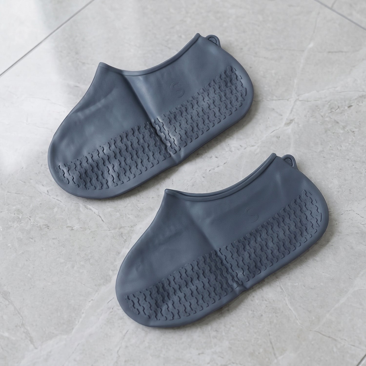 Two navy blue silicone shoe covers are laid flat on a light grey tiled surface, showcasing their textured soles.